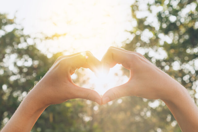 Female hands heart shape on nature bokeh sun light flare and blu