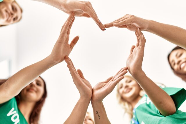 Group of young volunteers woman smiling happy make heart symbol with hands together at charity center.